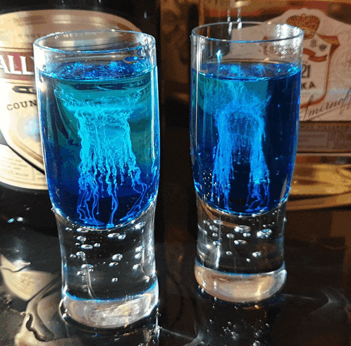 two shot glasses filled with blue liquid next to a bottle