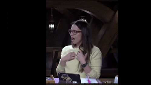 a woman wearing glasses and a yellow sweater is sitting at a table with her hair in her hand .