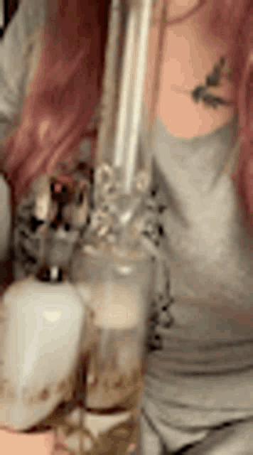 a woman with pink hair is smoking a bong with a tattoo on her chest .