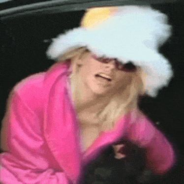 a woman wearing a white hat and sunglasses is standing in a car