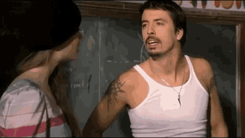 a man in a tank top is talking to a woman in a classroom .