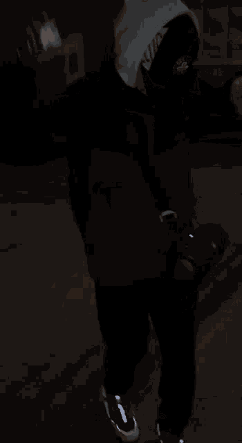 a person wearing a black jacket and a white hat is walking down a street at night .