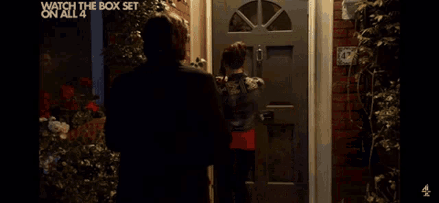 a man and a woman are standing in front of a door that says " watch the box set on all 4 "