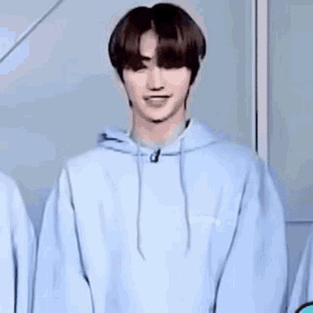 a young man in a light blue hoodie is standing in front of a wall and smiling .