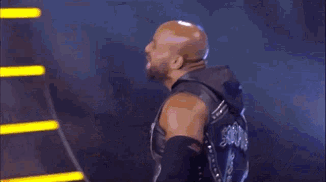 a wrestler is standing in a ring wearing a black vest and knee pads .
