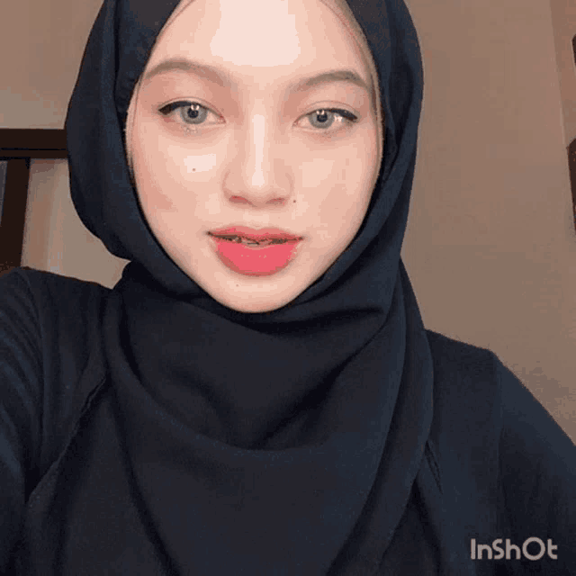 a woman wearing a black hijab is taking a selfie with an inshot watermark