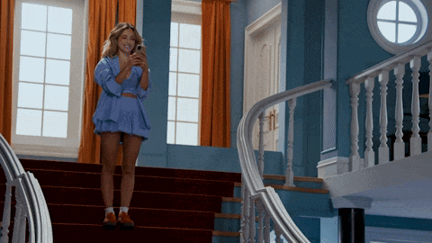 a woman in a blue dress stands on a set of stairs looking at her phone