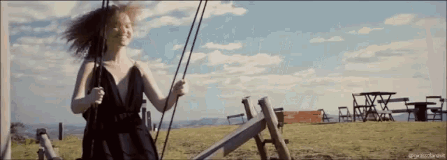 a woman in a black dress is swinging on a wooden swing in a field .