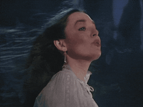 a woman in a white shirt and earrings looks up