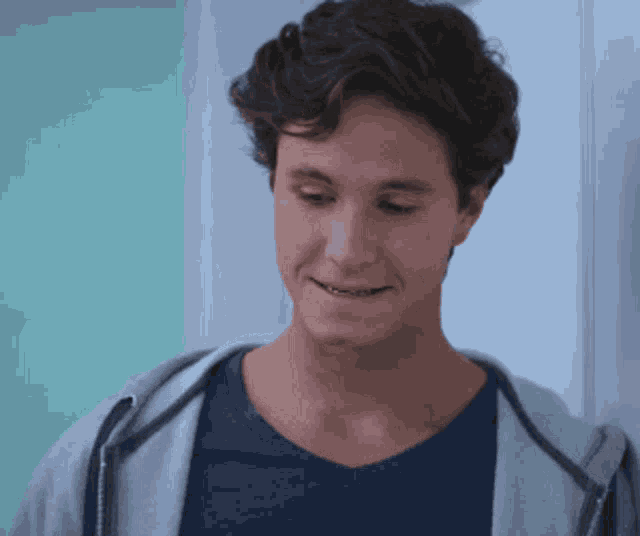 a young man wearing a gray hoodie and a blue shirt smiles