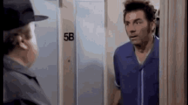a man in a blue shirt is standing in front of a door talking to another man .