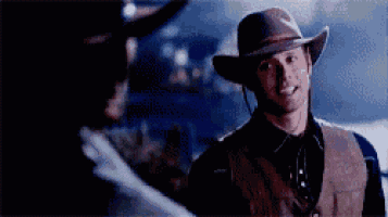 a man in a cowboy hat and vest is smiling while standing next to another man .