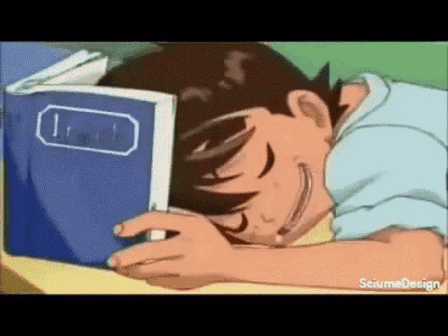 a boy is sleeping on a desk with a book on top of his head .