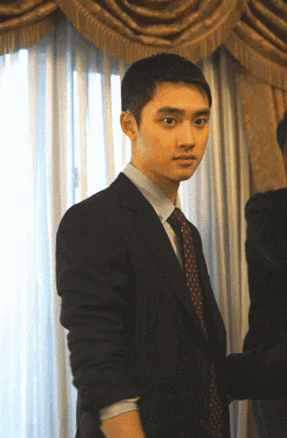 a young man in a suit and tie stands in front of a window