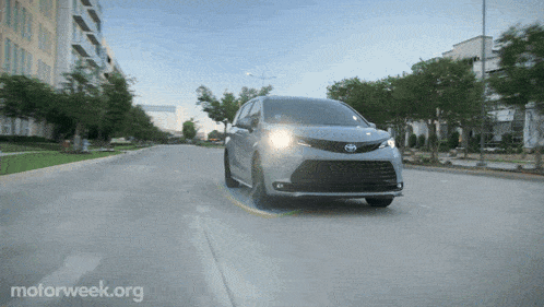 a toyota minivan is driving down a city street with motorweek.org written on the bottom