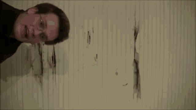a man wearing glasses is standing in front of a wall with a hole in it .