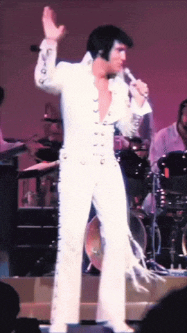 a man in a white suit is singing into a microphone on stage