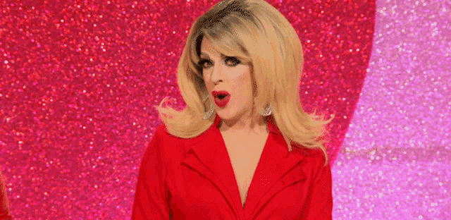 a drag queen is wearing a red jacket and making a surprised face .