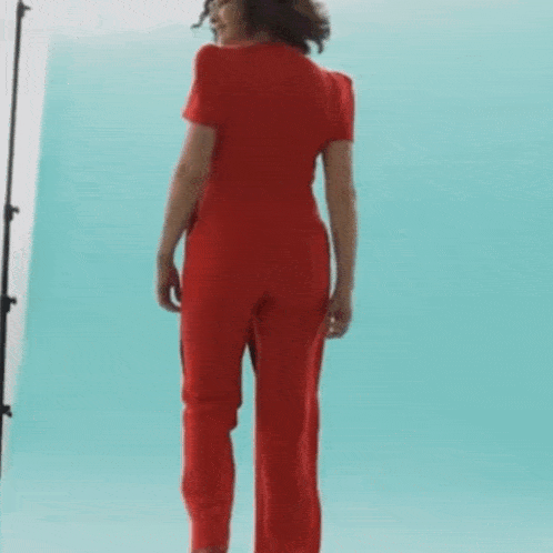 a woman is wearing a red jumpsuit with a black belt around her waist .