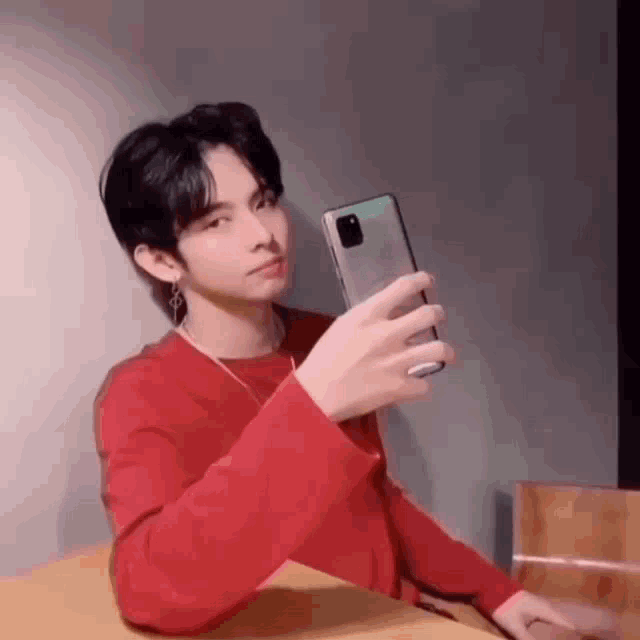 a man in a red shirt is taking a selfie with his phone .