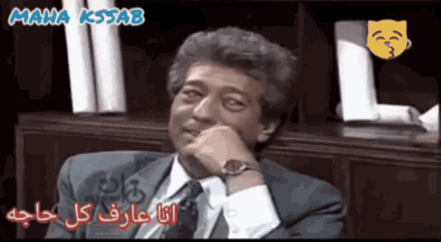 a man in a suit and tie sits in front of a maha kssab logo
