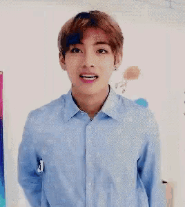 a young man in a blue shirt is standing in front of a wall with balloons on it .