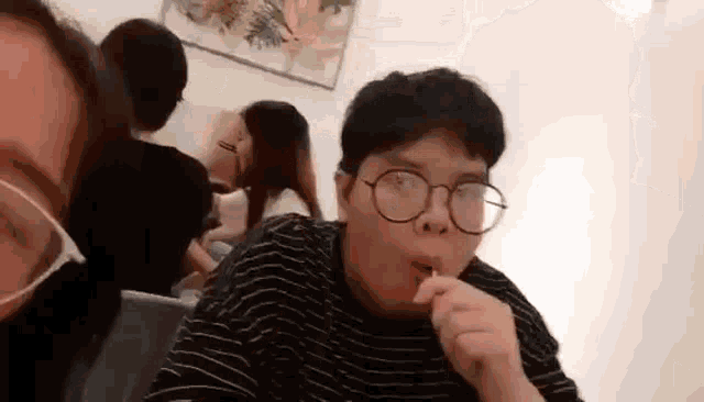 a man wearing glasses and a mask is sitting at a table eating a sandwich .