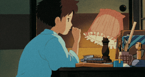 a boy in a blue shirt is sitting at a desk looking at a lamp