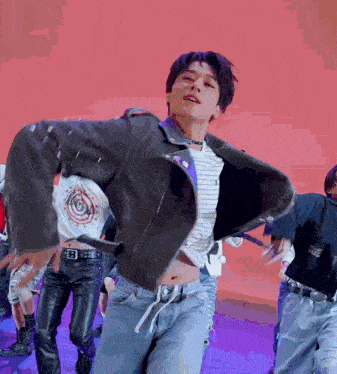 a man in a striped shirt and a black jacket is dancing in front of a pink background