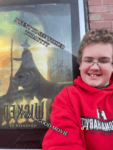 a boy wearing a red hoodie stands in front of a wicked movie poster