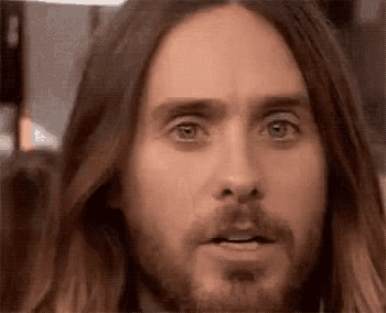 a close up of a man with long hair and a beard making a funny face .