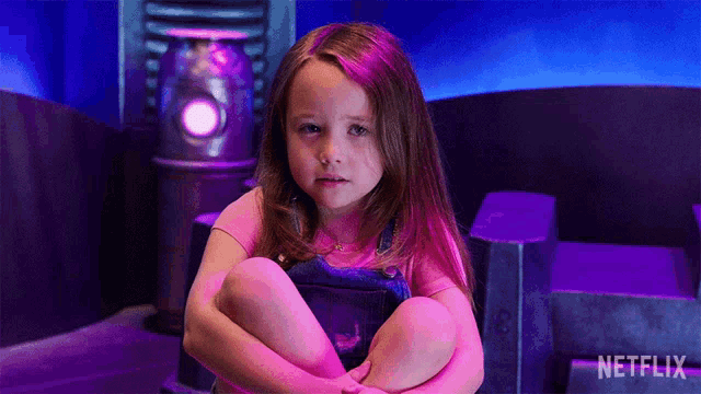 a little girl is sitting on the floor with her legs crossed in front of a netflix logo .