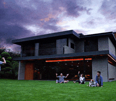 a group of people sit on the grass in front of a large house