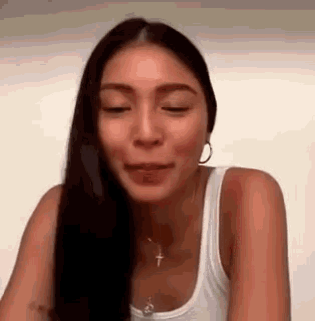 a woman with long hair is wearing a white tank top and a necklace .