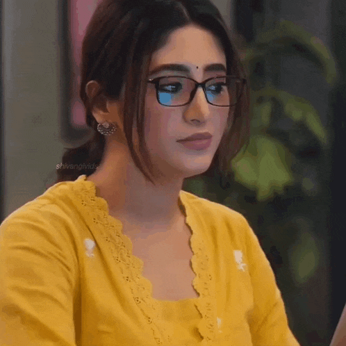 a woman wearing glasses and a yellow shirt is sitting in front of a laptop computer .