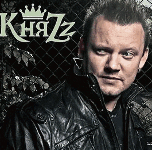 a man in a black leather jacket stands in front of a chain link fence with the word kna7z