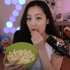 a woman is eating popcorn in front of a microphone in a green bowl .