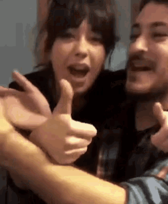 a man and a woman are giving a thumbs up sign .