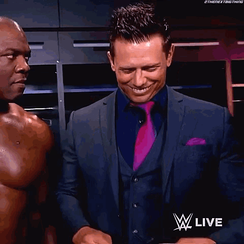 a man in a suit and tie is standing next to a shirtless man .