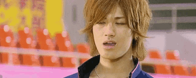a young man with long hair is wearing a blue jacket and necklace .