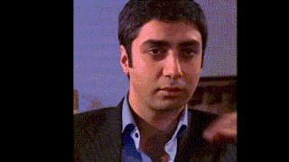 a man in a suit and blue shirt is making a funny face with his hand on his face .