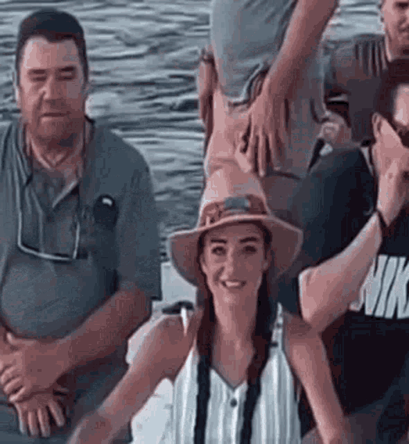 a group of people are sitting on a boat in the water . the woman is wearing a hat and smiling .