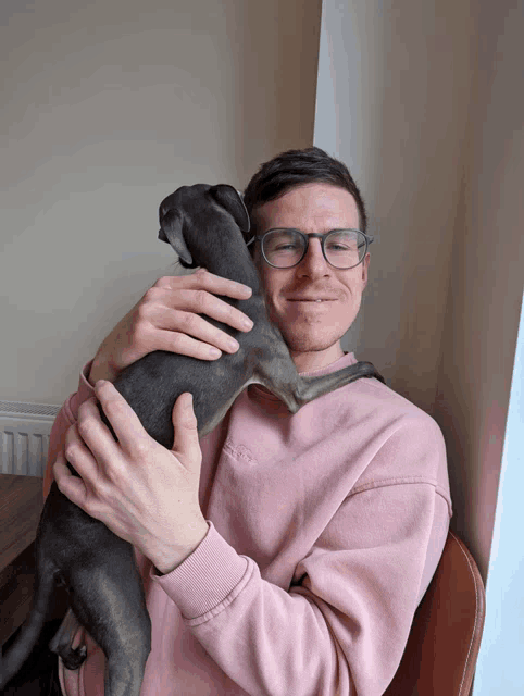 a man in a pink sweatshirt is holding a grey dog