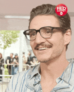 a man with glasses and a mustache is smiling in front of a red carpet advertisement