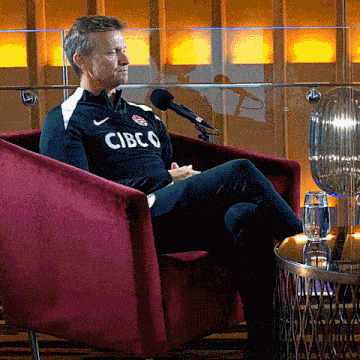 a man is sitting in a chair wearing a cibco shirt