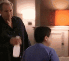 a man is holding a spray bottle and talking to another man in a blue shirt .