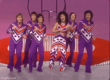 a group of people are dancing together on a stage in purple and red outfits .