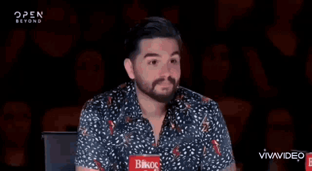 a man with a beard is sitting in front of a crowd in a chair .