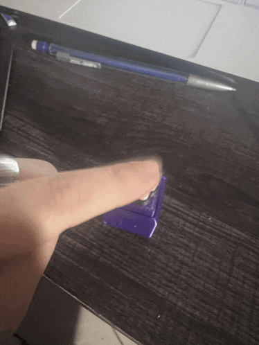 a person 's finger is pointing at a purple object on a desk