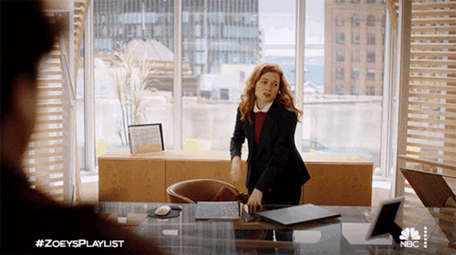 a woman in a suit is standing at a desk with a laptop on it and #zoeysplaylist on the bottom